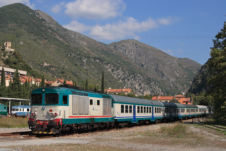 Arrivée en gare de Breil-sur-Roya du train régional 22977 Cuneo - Taggia, tracté par le D445 1104. Au fond, on aperçoit le matériel de l'Écomusée de Breil, dont notamment le X 2804 et la CC 7140.