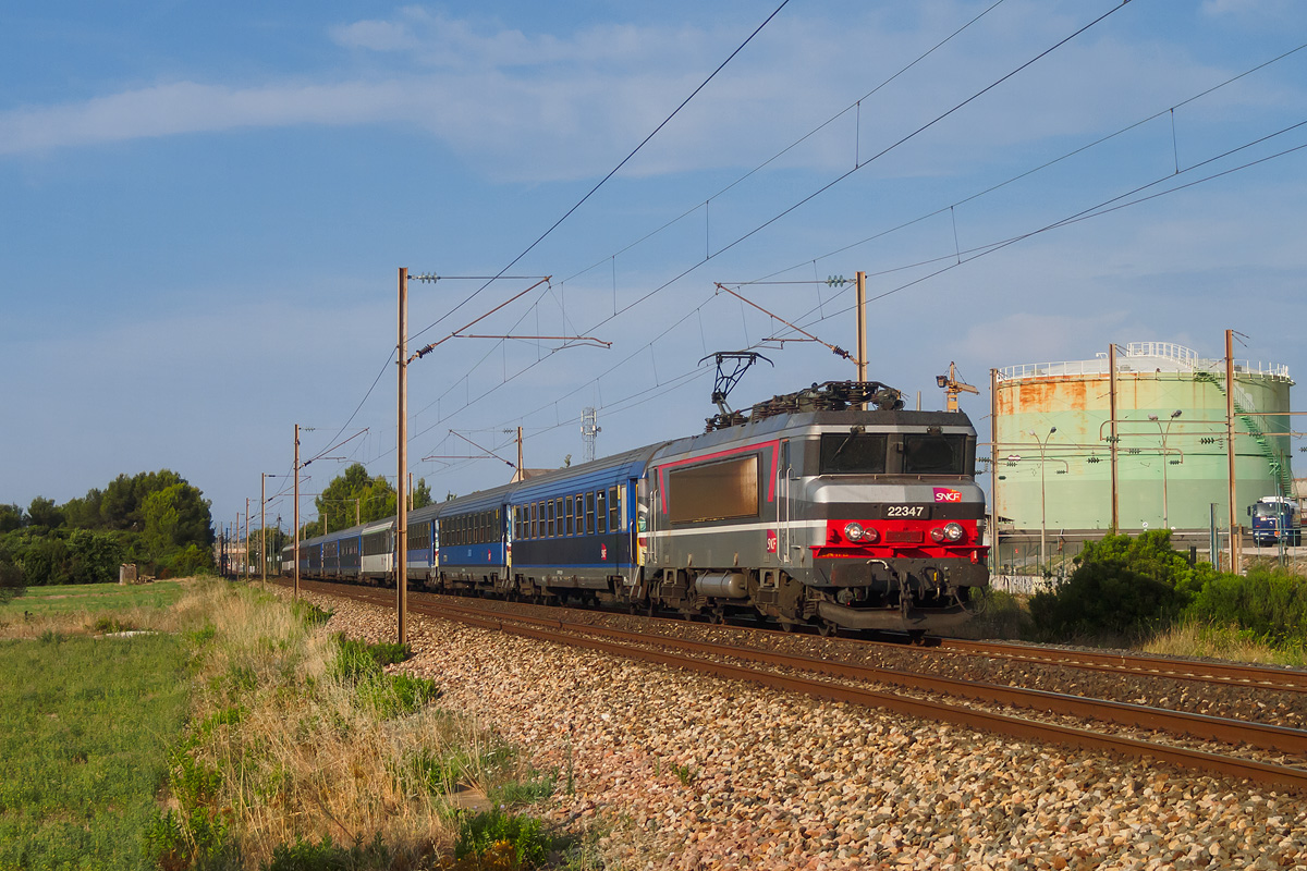 La BB 22347 est à la traction du train 5771 dit Train Bleu en ce matin du samedi 19 juillet 2014. Le train est vu au passage au PK 78,5, dans la commune de La Garde, peu de temps après avoir franchi la gare de La Pauline et quelques mètres avant l'embranchement privé de PétroGarde. Il se rapproche tranquillement et à peu près à l'heure de son terminus Nice Ville, qu'il atteint après onze heures de trajet depuis sa gare d'origine Paris-Austerlitz.