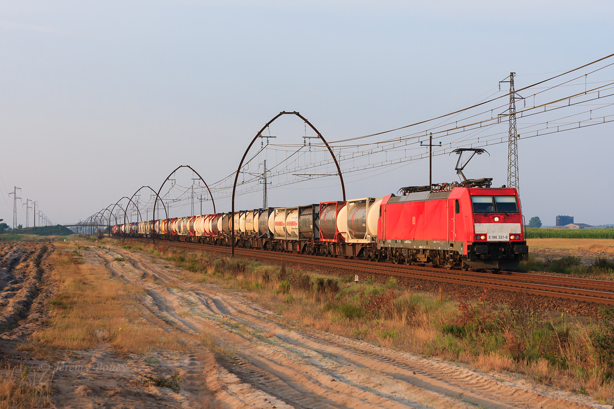 Alors que le Soleil sort enfin d'une légère brume matinale, la E 186 321-6 aux couleurs rouges de la Deutsche Bahn est vue au sud de Ychoux, dans les Landes, sur le 41210 Bayonne - Stiring-Wendel.