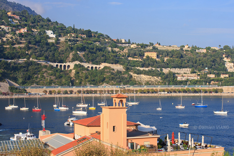 Ce train de p&egrave;lerins reliant Lourdes &agrave; l'Italie, tract&eacute; par la BB 22240 en livr&eacute;e "fant&ocirc;me", traverse la baie de Villefranche-sur-Mer ; au premier plan se trouve le b&acirc;timent de la Capitainerie.