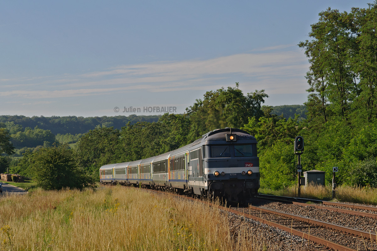 Par une soirée estivale, en cette fin du mois de Juin 2011, la BB 67514 emmène le TER 830939 vers Strasbourg. Elle passe ici à Zetting, peu après son départ de Sarreguemines (57).