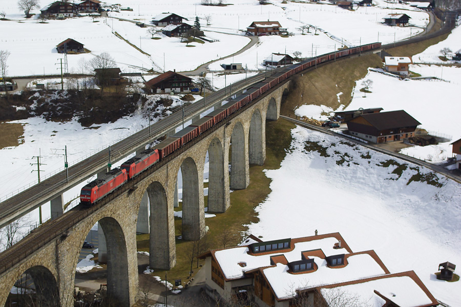 Sur la rampe nord du Loetschberg, sur le viaduc de la Kander, &agrave; Frutigen, dans le canton de Berne, une UM2 de BR 185 DB emm&egrave;ne vers le nord, une rame de tombereaux type Taems, dans un paysage enneig&eacute;.