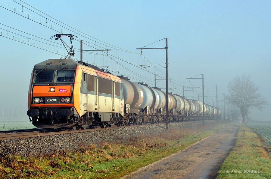 Remorquant un Modane - Miramas, la BB 26206 traverse la plaine de l'Ain par un matin brumeux. Le convoi vient de br&ucirc;ler la gare Meximieux et se dirige droit sur Lyon.