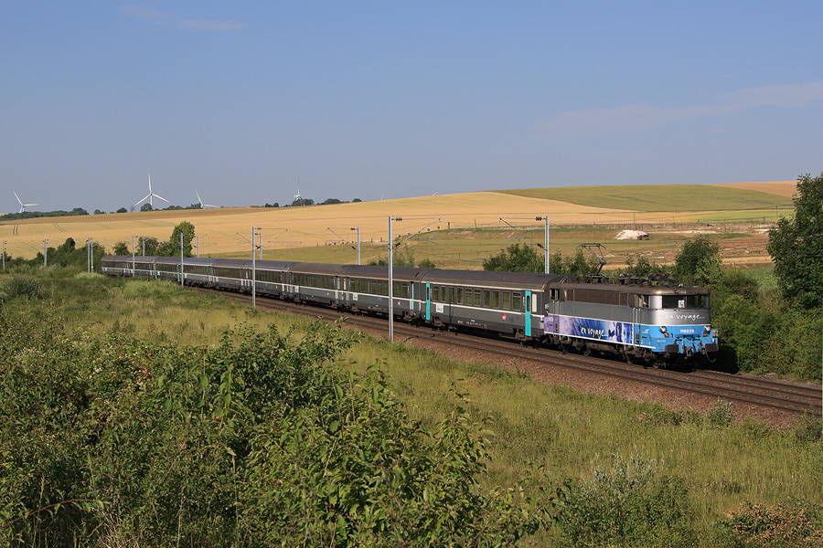 Passage &agrave; La Faloise, sur fond d'&eacute;oliennes, de l'InterCit&eacute;s 12038 Amiens - Paris-Nord. Il est emmen&eacute; par la BB 16039 remorquant une belle rame de voitures Corail+.
