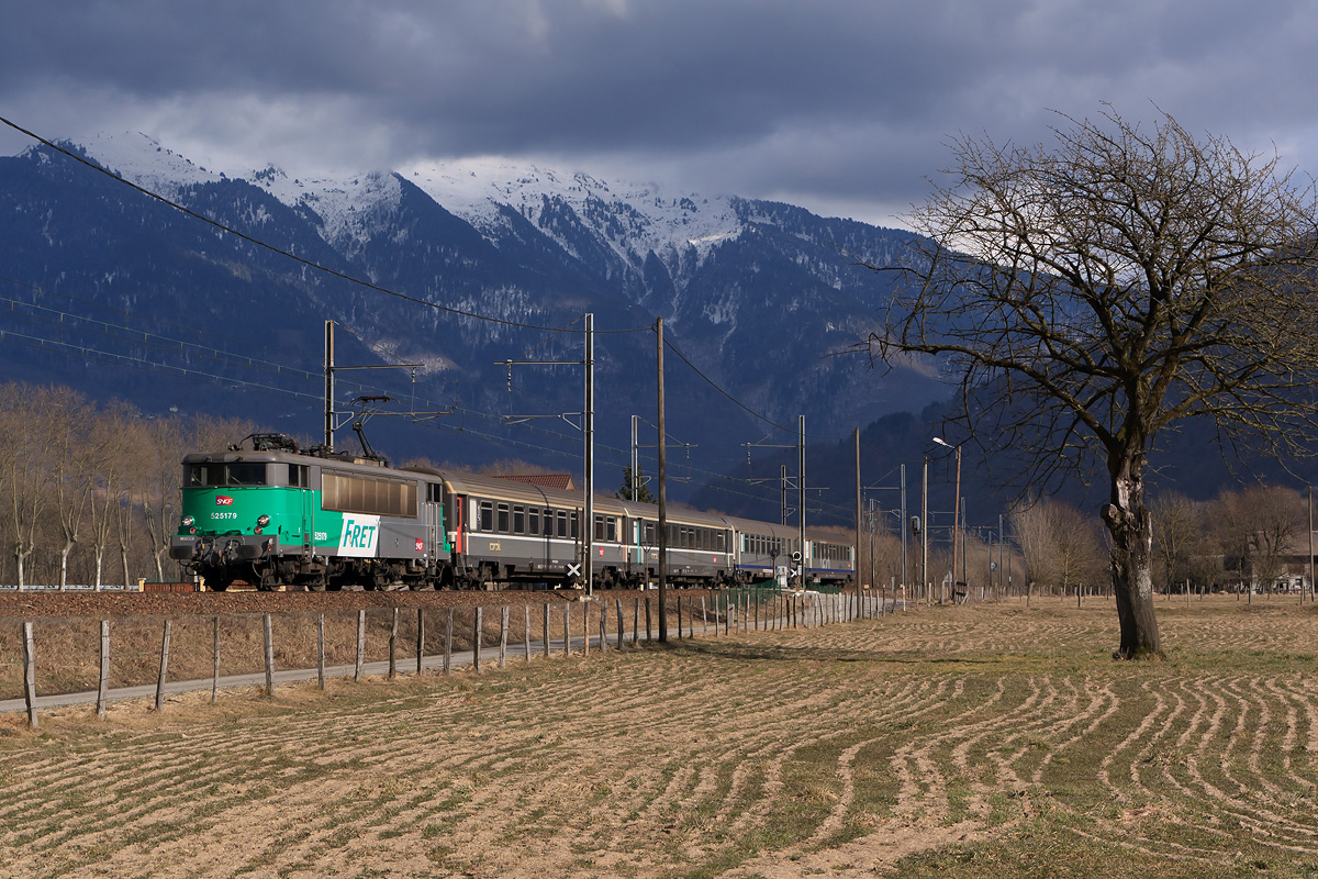 Sur fond de gros nuages noirs accrochés aux montagnes, la BB 25179 redescend de Modane, avec un TER à destination de Chambéry.