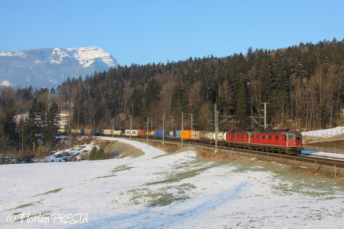 Alors que la journée commence, une Re 12/12 rouge (UM de Re 6/6) assure la traction de ce train combiné à destination de l'Italie par l'itinéraire du Gotthard.