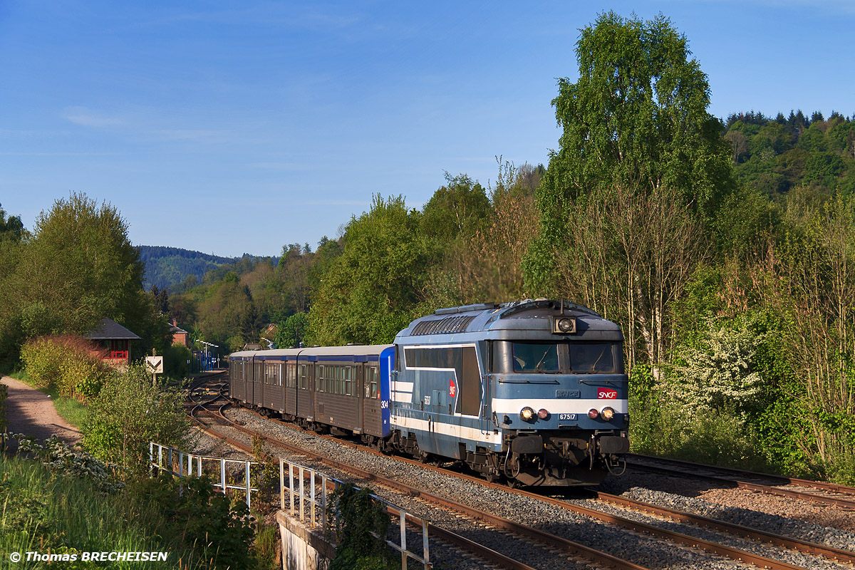 La BB 67517 avec la RRR 304 viennent de quitter la gare de Rothau dont on peut voir le bâtiment au fond. Elles assurent le TER 831881 en direction de Strasbourg.