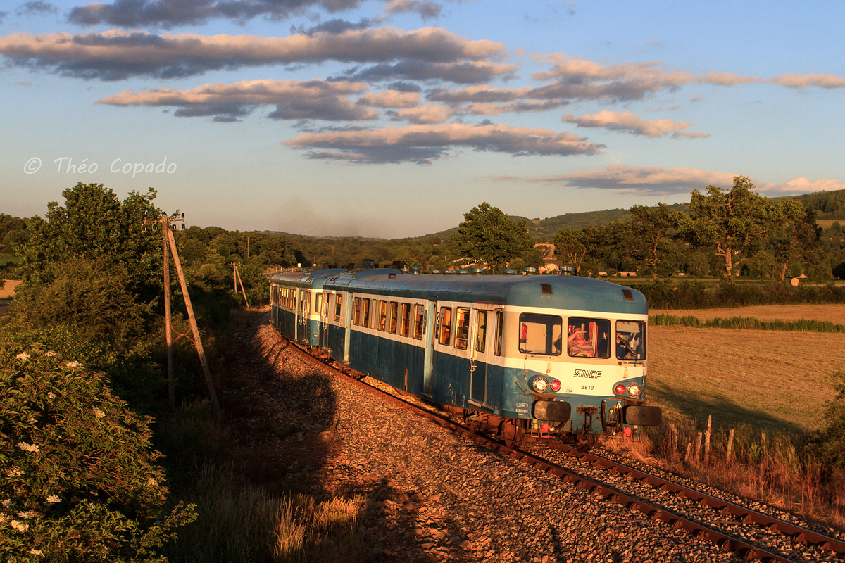 Début des années 2000, c'est par une lumière de feu que les X 2819 et 2914 en UM dans leur belle livrée bleu d'Auvergne sont vus assurant un train de soirée sur la petite ligne Sévérac-le-Château - Rodez encore dans son jus avec ses poteaux télégraphiques et son rail DC du midi.