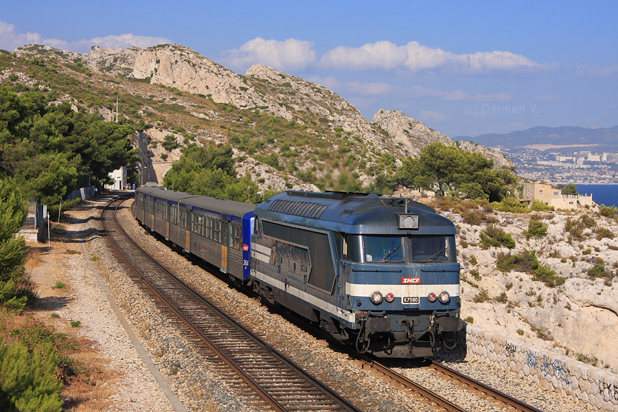 La BB 67580, de nouveau plaquée, et la RRR 264 quittent la gare de Niolon, entre mer et falaises, assurant le TER 879766 entre Marseille et Miramas.